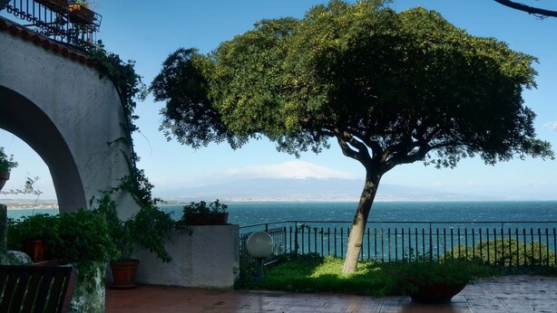 Een patio met bomen, uitzicht op zee en een bergketen in de verte.