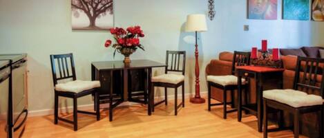 A dining area with a table and chairs, a vase with flowers, a lamp, and a sofa.