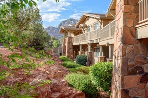 A hotel with a stone facade, multiple balconies, and a mountainous backdrop. - Sedona | Couples Canyon Stay | Pool + Hot Tub (Sedona)