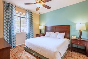 Una habitación de hotel con una cama, dos mesitas de noche con lámparas, un ventilador de techo y una ventana con cortinas.
