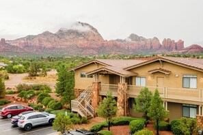 Un hotel de dos pisos con fachada de piedra, un balcón y un estacionamiento con coches.