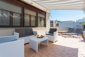 A patio with outdoor furniture, including a sofa, chairs, and a table with a plate and glasses.