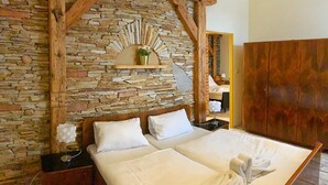 A double bed with white linens, a stone wall, wooden beams, a small shelf with a plant, and a wooden wardrobe. - Hotel World of Harmony (Lánov)