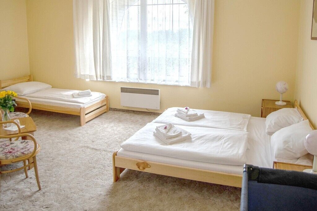 A room with two single beds, a small table with chairs, a window with curtains, and a radiator.
