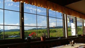 A restaurant with large windows offering a view of a green landscape and distant hills. - Hotel World of Harmony (Lánov)