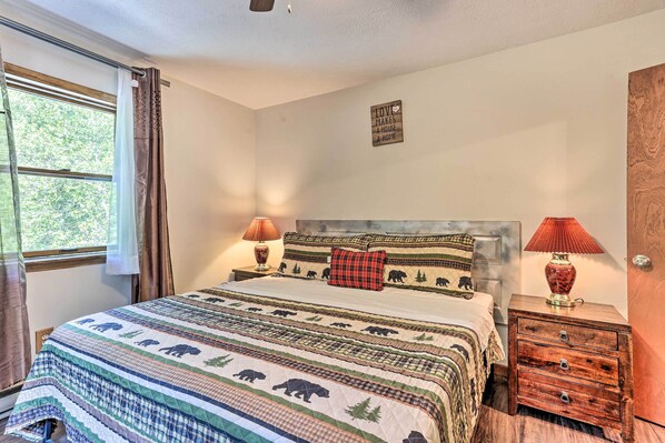 A bedroom with a bed, two nightstands, a window with curtains, and a wall sign.