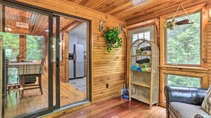 A wooden interior with a glass door leading to a dining area, a leather sofa, and a shelf with folded items.