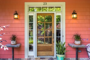 A wooden door with glass panels, flanked by two potted plants on either side, and a number '23' above the door. - Grey River Gatherings (perfect for large groups) (Woodfin)
