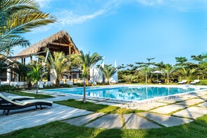 A pool area with lounge chairs, a thatched-roof structure, and tropical vegetation. - Coconut Paradise Beach Villa (Juan Baron)