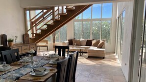 Amplia sala de estar con una escalera de madera, un sofá grande y una mesa de comedor lista para cuatro comensales.