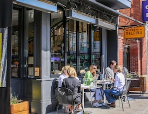 Enjoy a meal in our outdoor seating area with large windows, metal chairs, and potted plants.