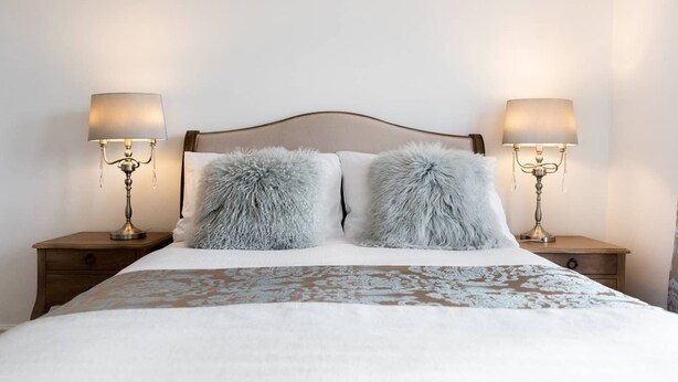 Una cama bien hecha con una colcha estampada, dos almohadas mullidas y dos lámparas de noche sobre mesitas de madera.