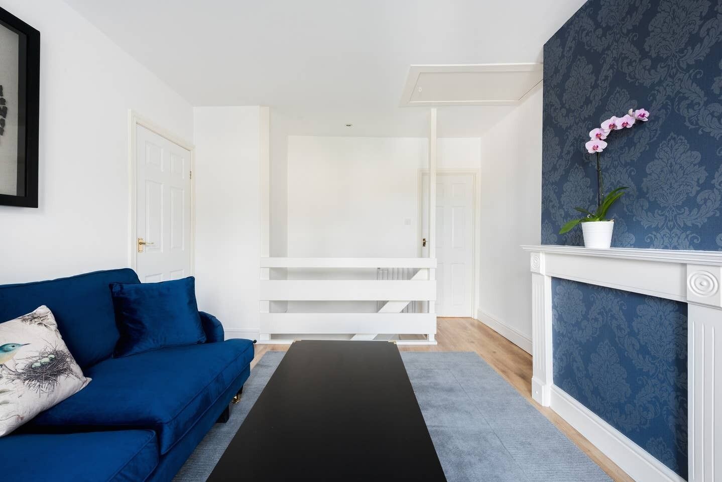 A modern living room with a blue sofa, a black bench, and a white fireplace with a blue patterned wall.