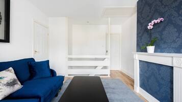 A modern living room with a blue sofa, a black bench, and a white fireplace with a blue patterned wall.