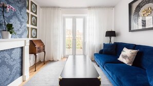 Un salón con un sofá azul, una mesa de centro negra, una mesita de noche de madera y una planta en maceta.