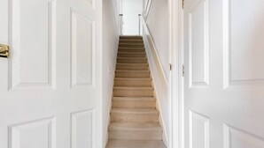 Un pasillo estrecho con puertas blancas y una escalera con alfombra que lleva a una habitación.