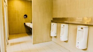 En offentlig toilet med tre pissoirer, en håndvask og en sæbedispenser på væggen.