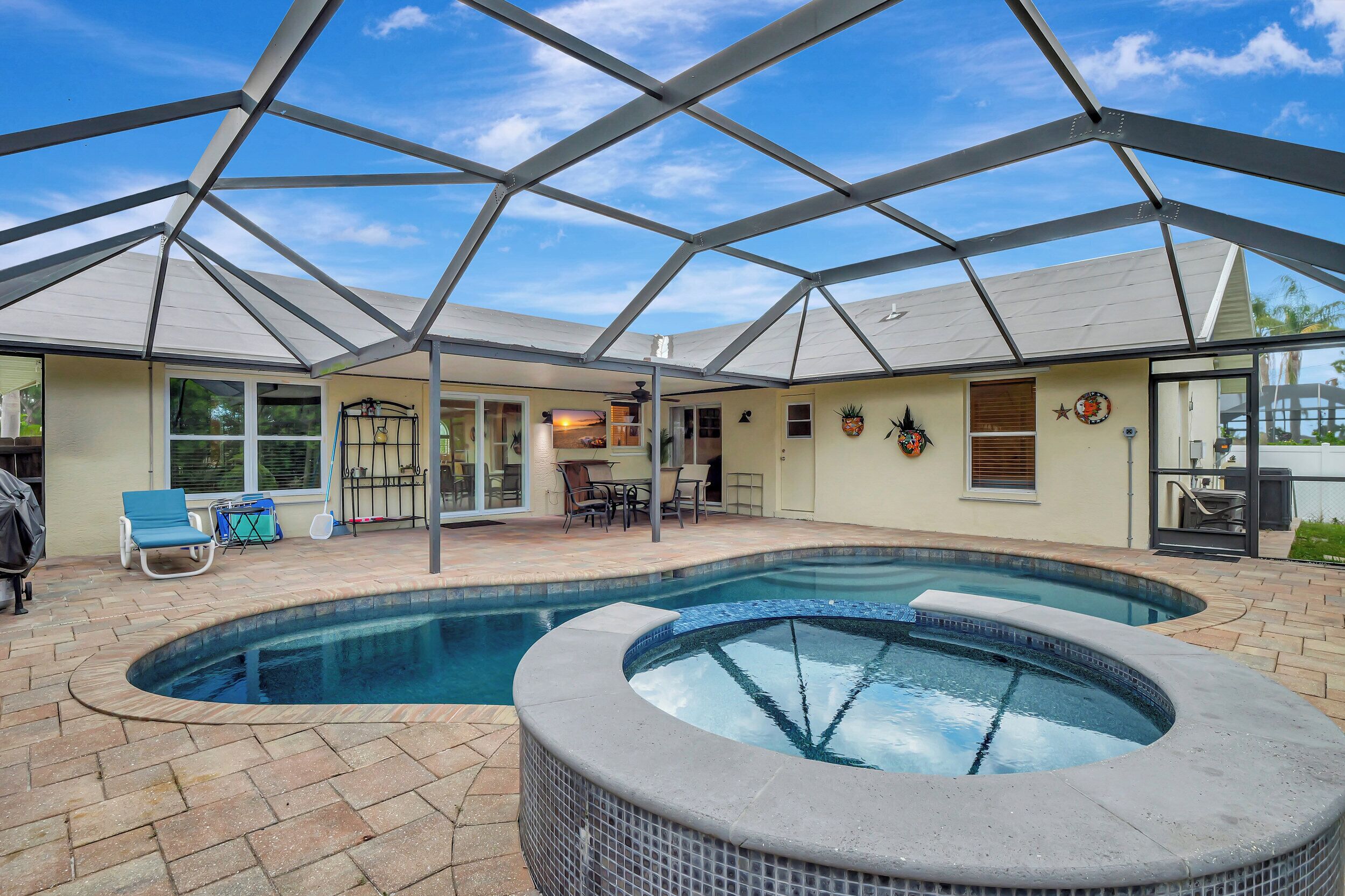 Un área de piscina exterior cubierta con jacuzzi, sillones reclinables y un patio con mesa y sillas.