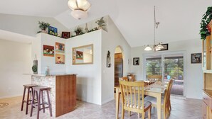 A kitchen with a central island, wooden bar stools, a dining table with chairs, and a view through a glass door to an outdoor area.