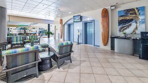Eine geräumige Lobby mit Korbmöbeln, einem Surfbrett und einem Palmenbaum-Gemälde.