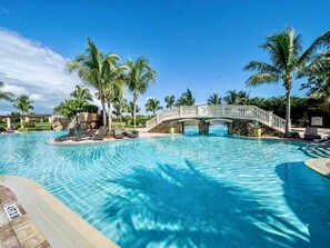Une piscine avec un pont, des palmiers et des chaises longues.