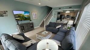 A modern living room with a sofa set, a coffee table, a TV, and a staircase leading to the kitchen. - Beachfront! Near Town! Views! Heated Pool! 5Bd/3Bth #7 (Gulf Shores)