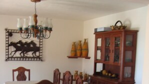 Ein Essbereich mit einem Tisch, gedeckt für vier Personen, umgeben von Holzstühlen. An der Wand steht eine Holzvitrine mit Glastüren, darüber hängt eine Chandelier.