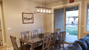 A dining area with a wooden table and chairs, a black leather couch, a hanging light fixture, and an 'EXIT' sign. - Beautiful Home near Zions with PRIVATE POOL, GAZEBO and GARAGE (La Verkin)