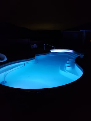 Swimmers can enjoy a refreshing dip in the pool's curved waters, surrounded by a central water feature and steps.
