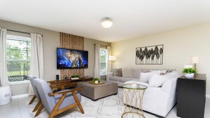 Un salon moderne comprenant un canapé, un pouf, une télévision et des objets de décoration.