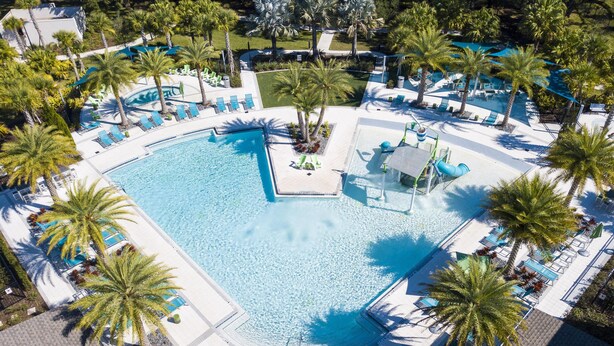 Vue aérienne d’un complexe hôtelier doté d’une piscine centrale, entourée de palmiers et de chaises longues.