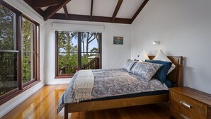 A bedroom with a wooden bed, a nightstand, a window with a view of trees, and a ceiling with exposed beams.