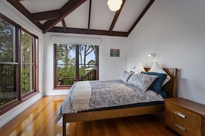 A bedroom with a wooden bed, a nightstand, a window with a view of trees, and a ceiling with exposed beams.