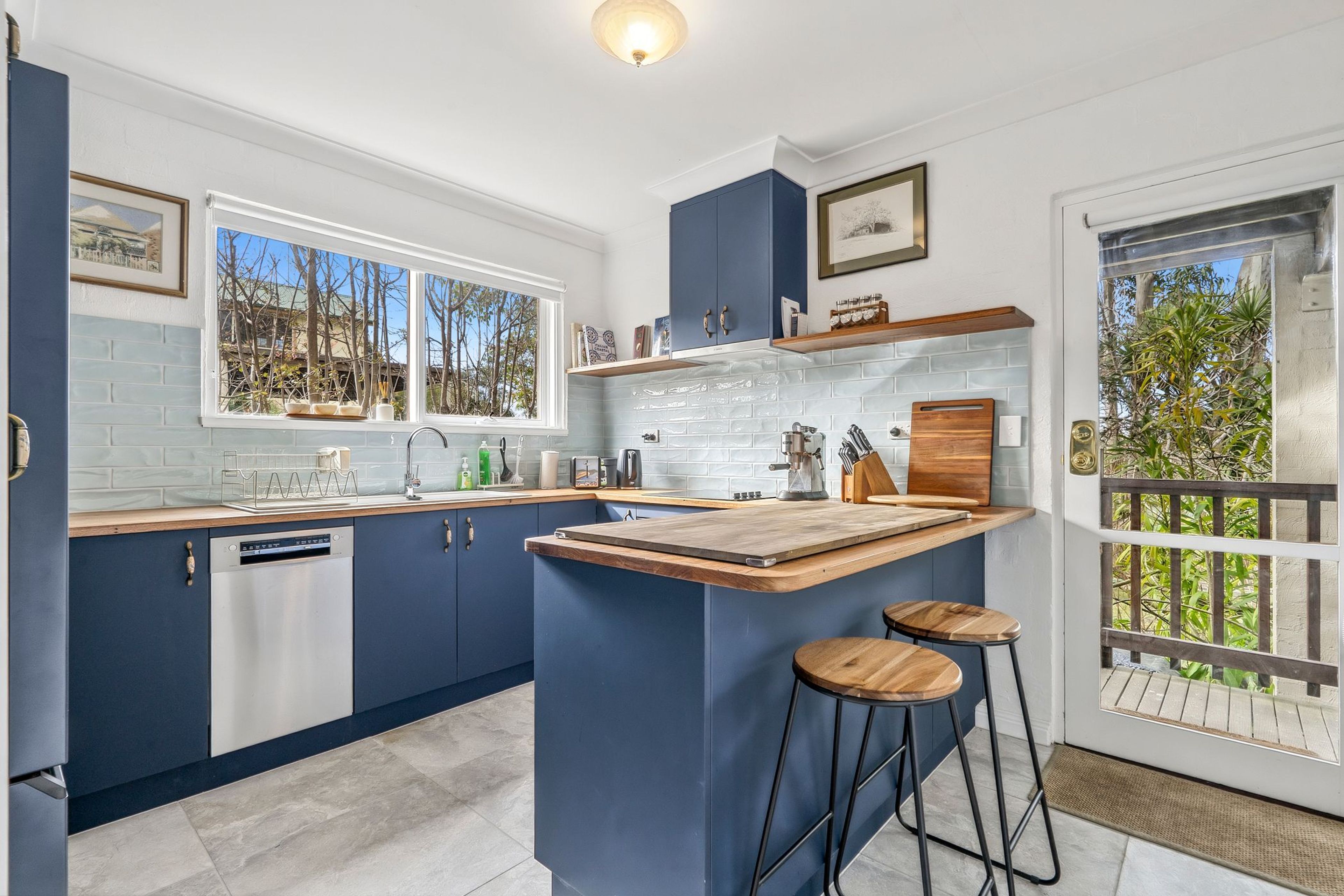 A modern kitchen with a central island, bar stools, and a view of the outdoors.
