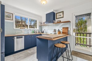 A modern kitchen with a central island, bar stools, and a view of the outdoors.
