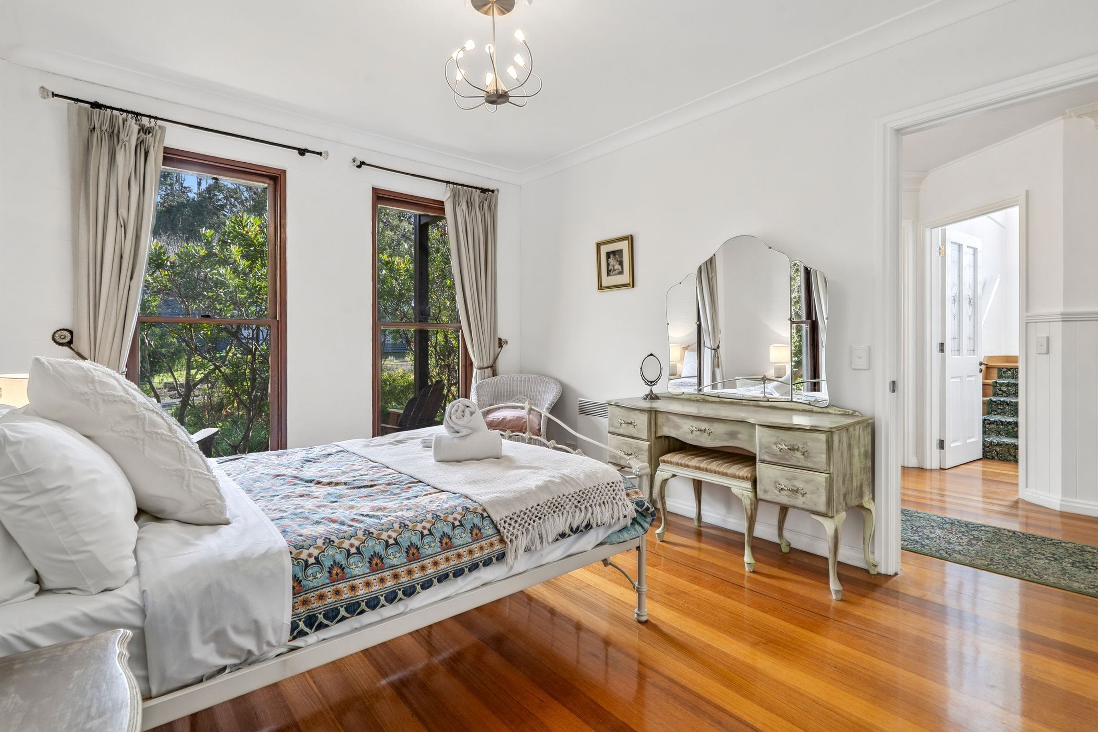 Une chambre à coucher avec un lit, une commode, un miroir et une fenêtre avec des rideaux.