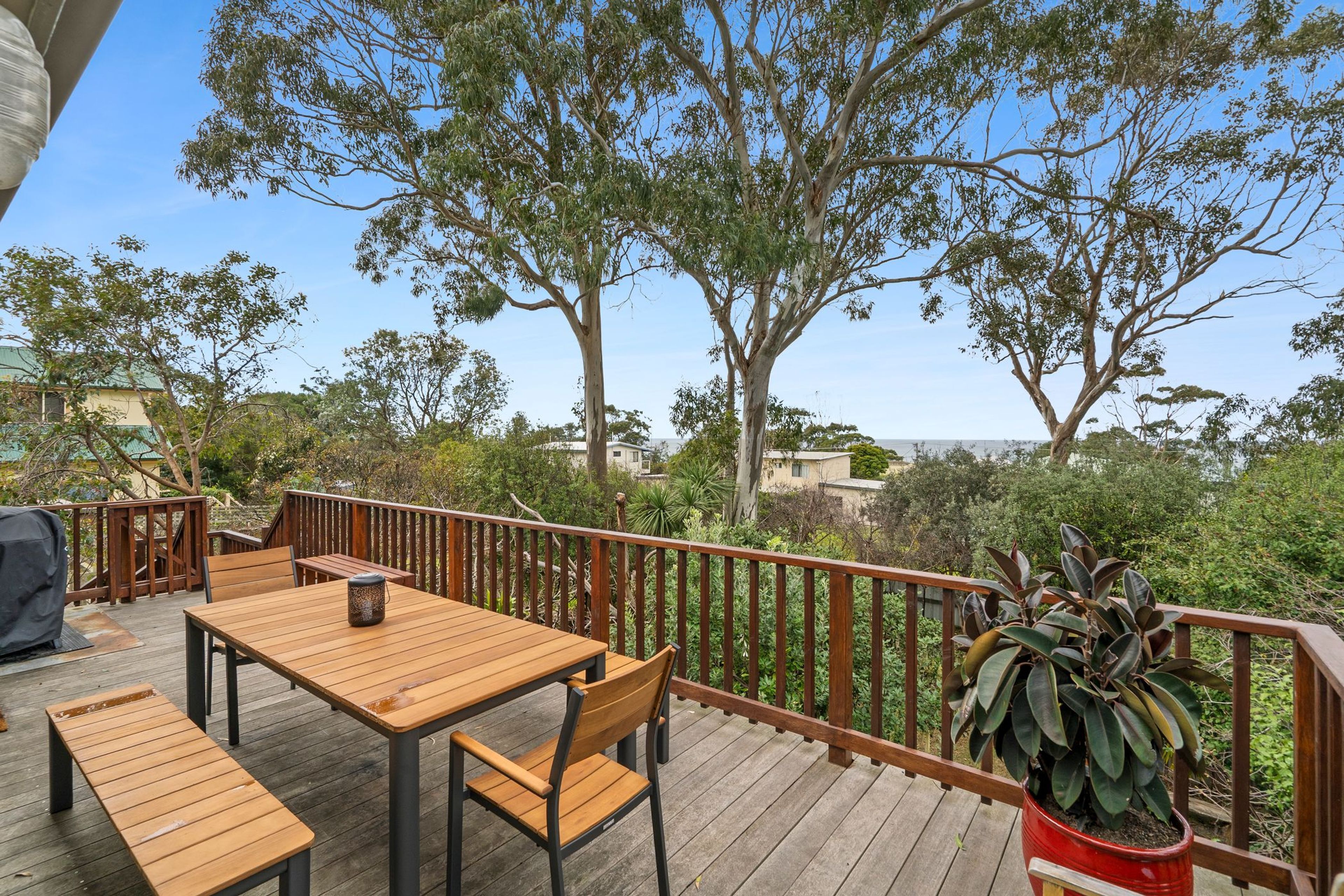 Une terrasse en bois avec une table et des chaises, entourée d’une balustrade en bois et agrémentée de diverses plantes.