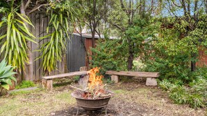 A backyard with a fire pit, a wooden bench, and various plants.
