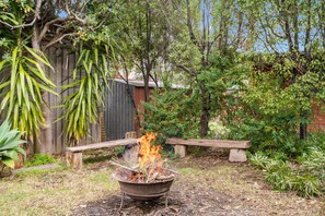 A backyard with a fire pit, a wooden bench, and various plants.