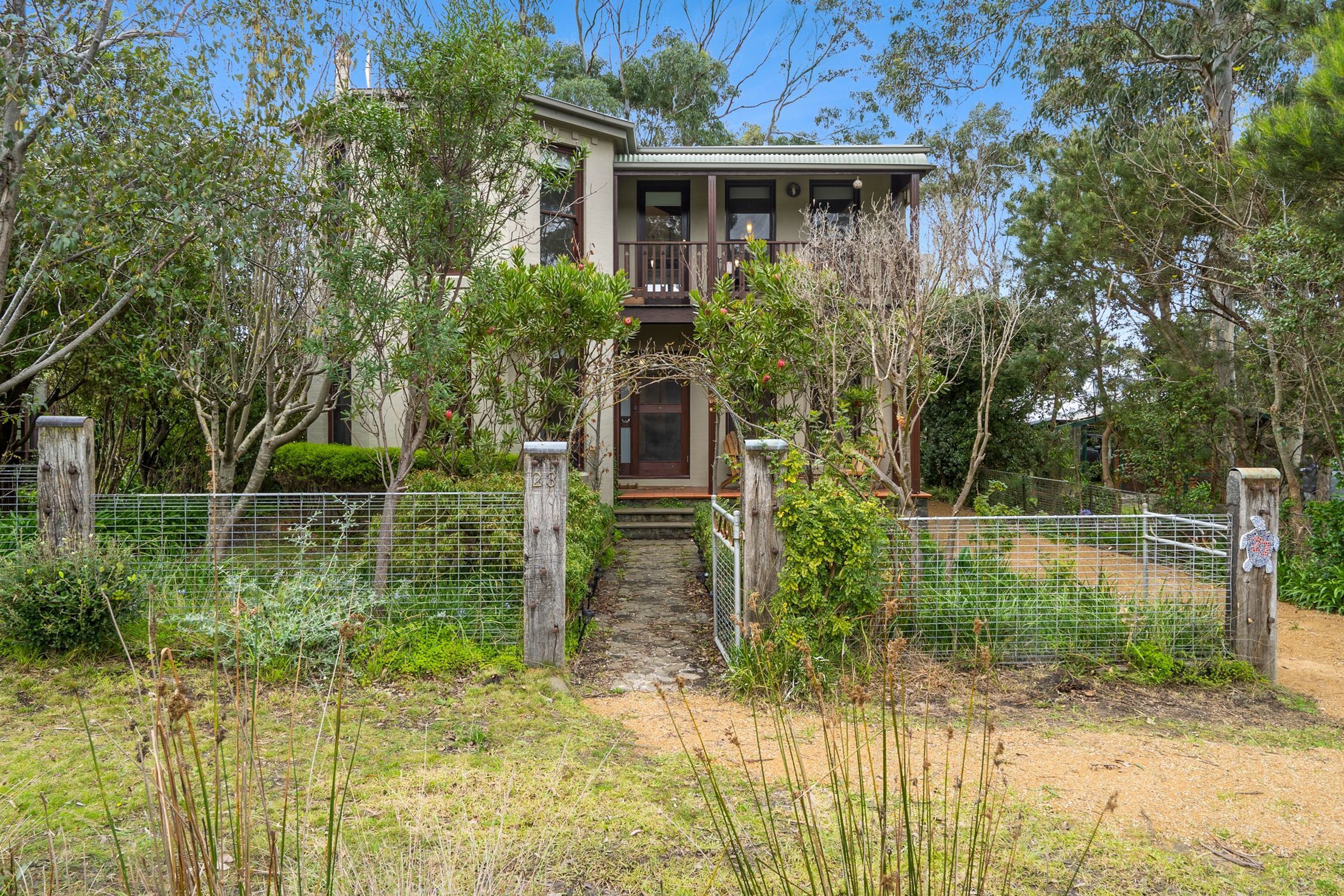 A two-story house with a front porch, surrounded by trees and a fenced yard.