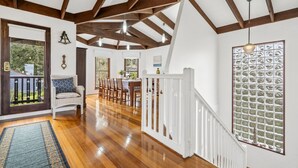 A spacious interior with wooden beams, a dining area, and a staircase leading to a balcony.