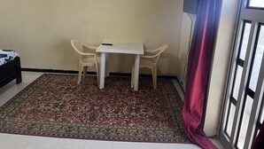Une petite pièce avec un lit simple, une table avec deux chaises, un tapis à motifs et une fenêtre avec un rideau.