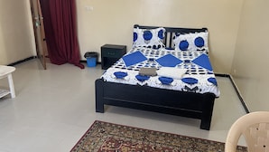 Un lit avec une couvre-lit à motifs, une petite table de chevet, une chaise, un tapis et un rideau.