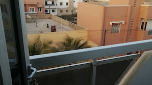 Une vue depuis un balcon doté d’une rambarde en métal, donnant sur un quartier résidentiel avec différents bâtiments et un ciel dégagé.
