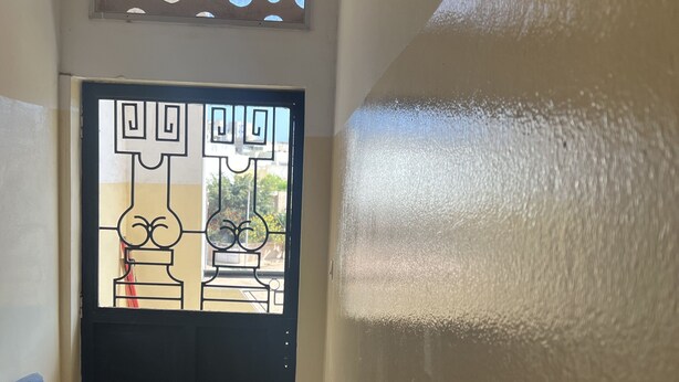 Un couloir avec une porte noire ornée de panneaux de verre décoratifs et d’un motif géométrique.
