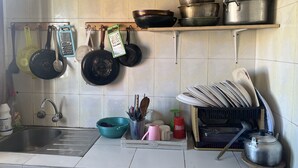 Une cuisine équipée d’un évier, de différents ustensiles de cuisine et casseroles suspendus au mur, d’un égouttoir et d’une bouilloire posée sur un plateau en bois.