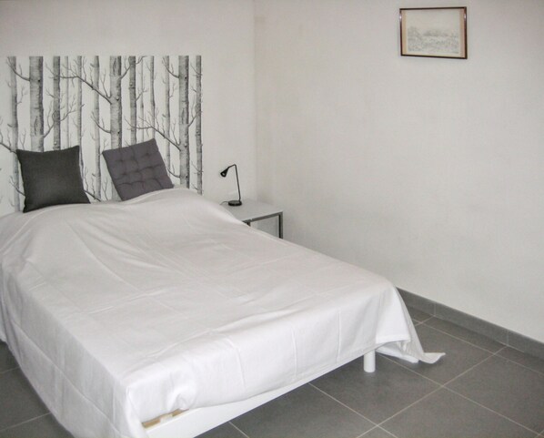 A neatly made bed with a white bedspread and two pillows, a bedside lamp, and a framed picture on the wall.