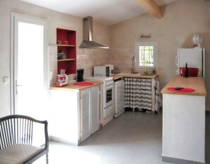 A compact kitchen with a built-in oven, microwave, and a small sink. There is a chair and a wooden table with a red mat.