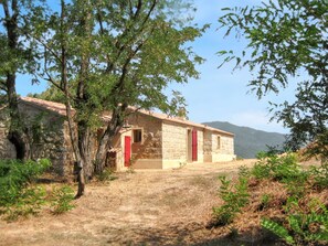 A stone building with a red door, surrounded by trees and dry grass, with mountains in the background.