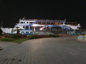 A large boat named 'NILE LOTUS' docked at a port with a paved walkway leading to its entrance. - Charming sunset,with Panoramic Nile view and pyramid view. (Cairo)
